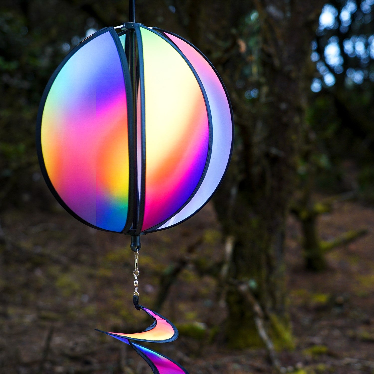 11-inch Jewel Hanging Ball Spinner with blended jewel design spinning in a garden, featuring six colorful panels and a 30-inch curlie tail.