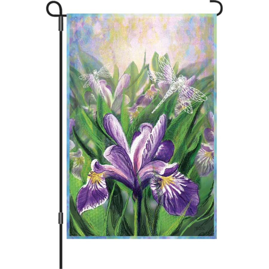 12 in. garden flag featuring a vibrant blue iris design, fluttering softly on a flagpole in a landscaped outdoor garden.
