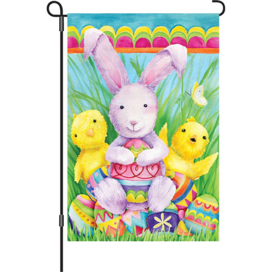12 in. Bunny and Friends garden flag featuring whimsical bunnies illuminated, displayed outdoors in a cheerful garden setting.