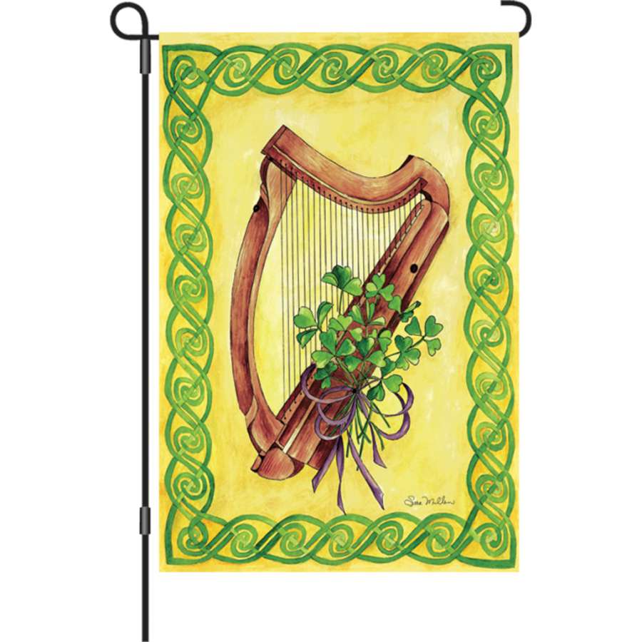 12 in. Celtic Harmony illuminated garden flag with intricate designs displayed in a garden setting at dusk, showcasing its vibrant colors.