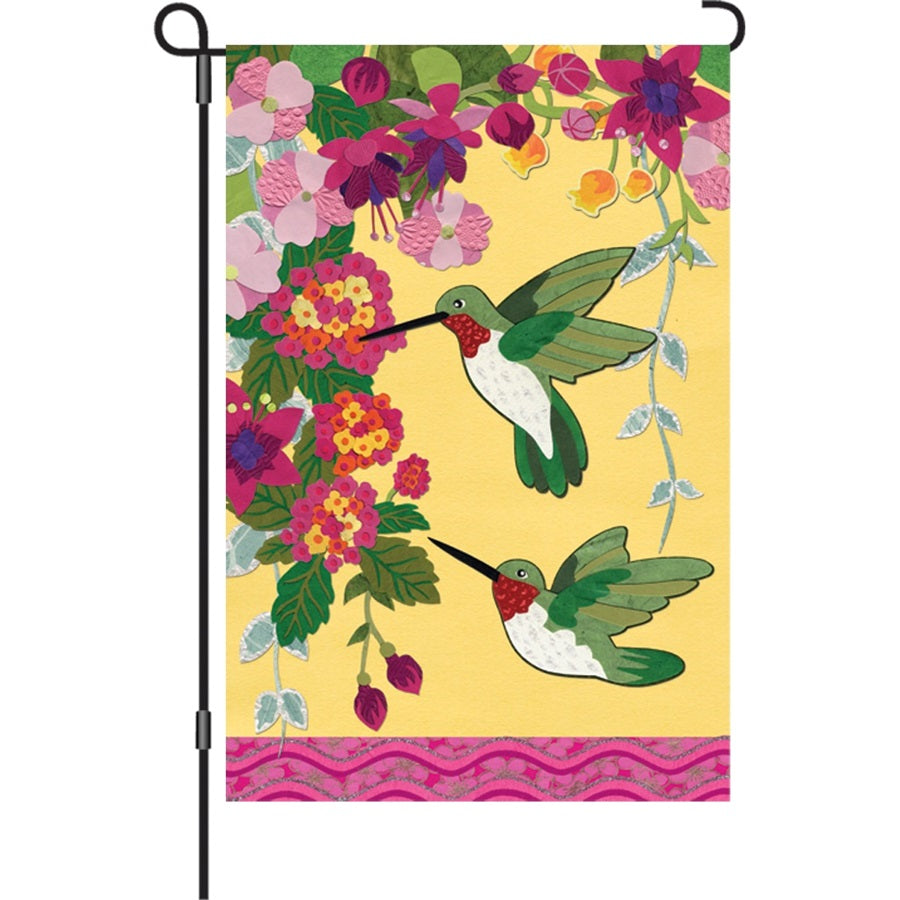 12 in. illuminated garden flag featuring colorful hummingbirds on a fuchsia background, displayed outdoors among flowers.