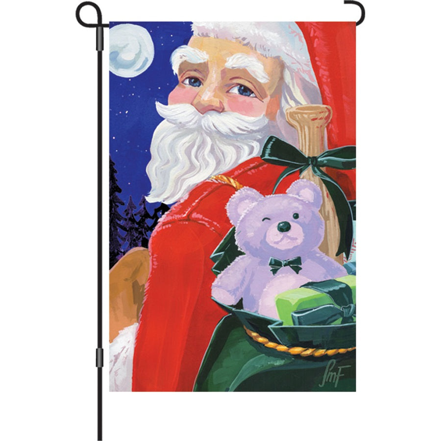 Illuminated 12 in. garden flag featuring Santa design, glowing softly in a winter landscape, adding festive charm to the outdoor setting.