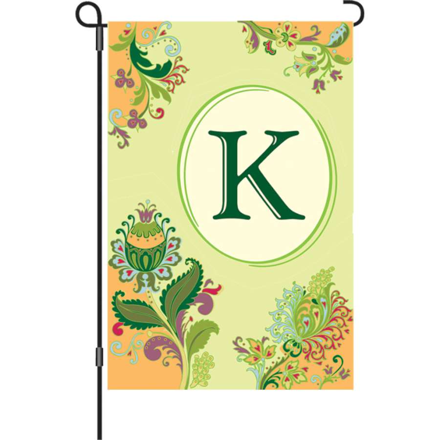 12 in. Spring Monogram Flag - K displayed in a garden, featuring a vibrant monogram design and weather-resistant fabric.