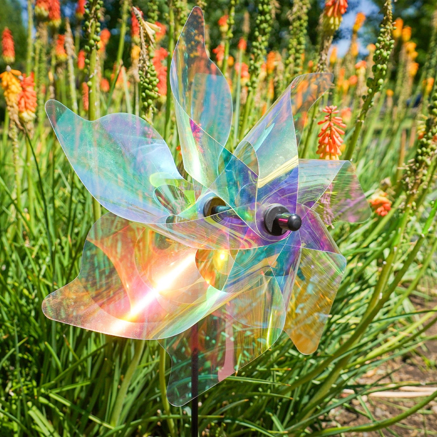 12-inch iridescent pinwheel spinner displayed in a garden, featuring colorful Mylar petals that catch the wind and reflect sunlight.
