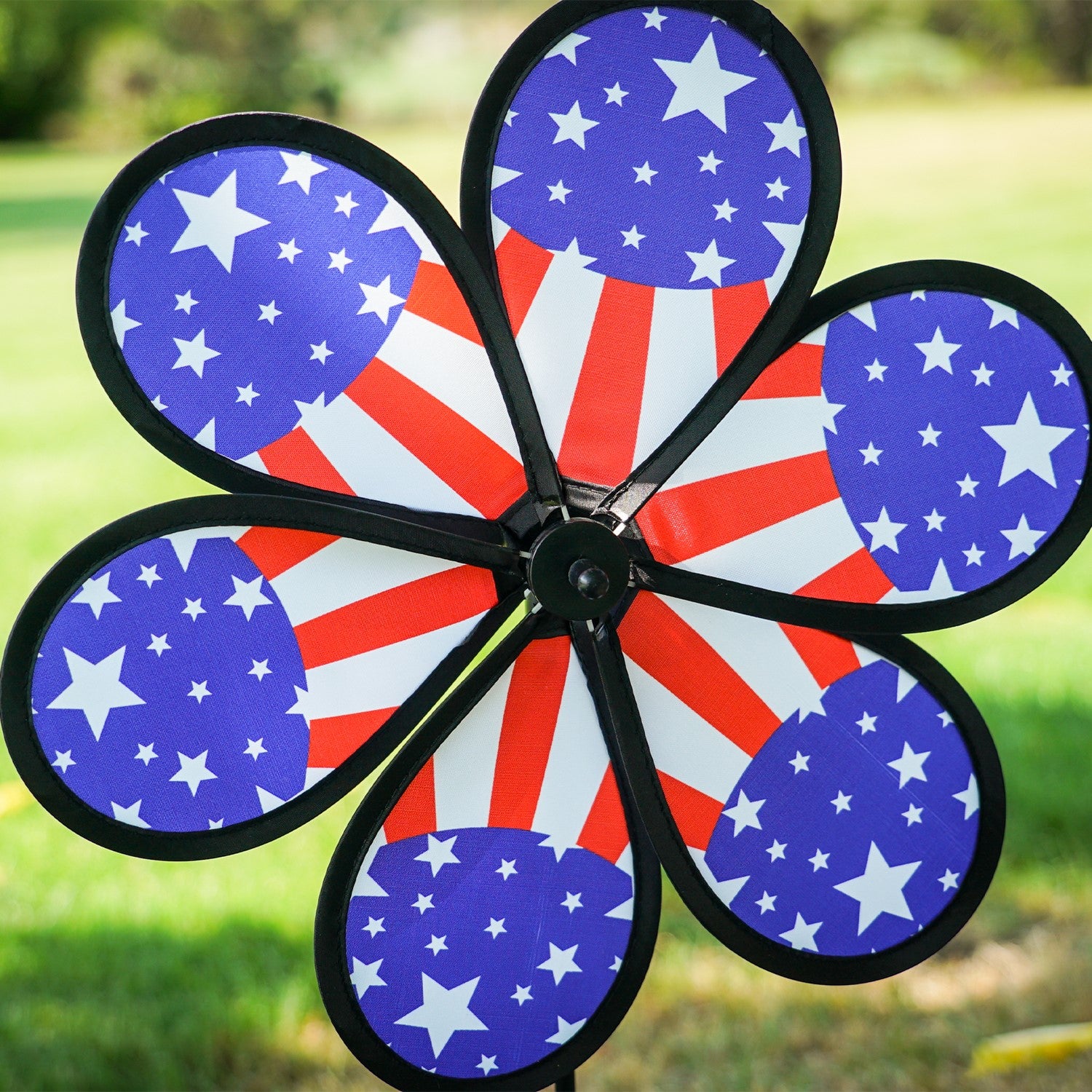 12-inch Patriot Star Flower Spinner with a vivid Stars and Stripes design, spinning on a garden pole in an outdoor setting.