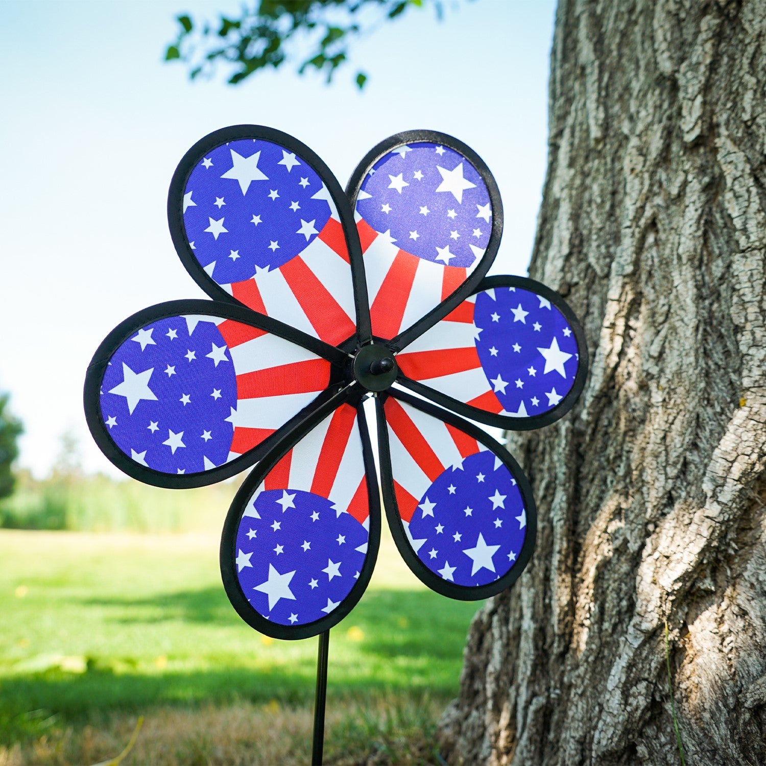 12-inch Patriot Star Flower Spinner with a vivid Stars and Stripes design, spinning on a garden pole in an outdoor setting.