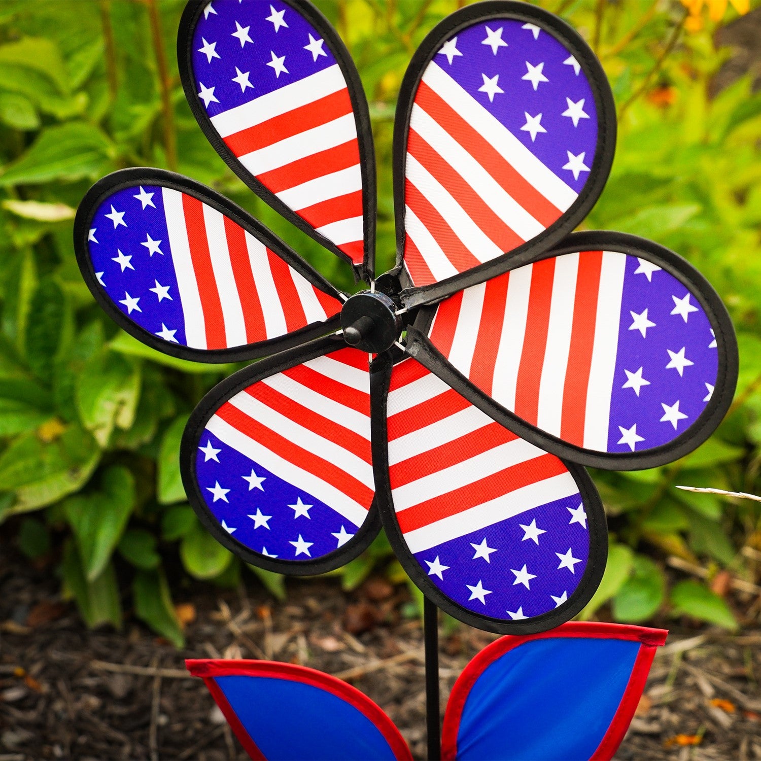 12-inch Patriotic Flower Spinner with stars and stripes petals, colorful leaves on a fiberglass stem, elegantly spinning in the breeze.