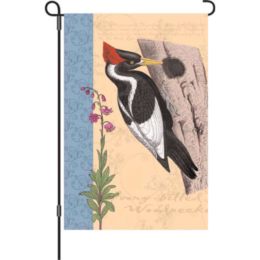 12-Inch Pecking In Woods garden flag with bird design among fall leaves displayed outdoors, illuminated for evening visibility.