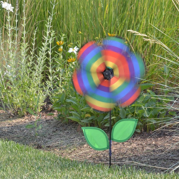 12-inch Rainbow Stripe Flower Spinner with vibrant petals and two leaves attached to a fiberglass pole, spinning in a garden setting.