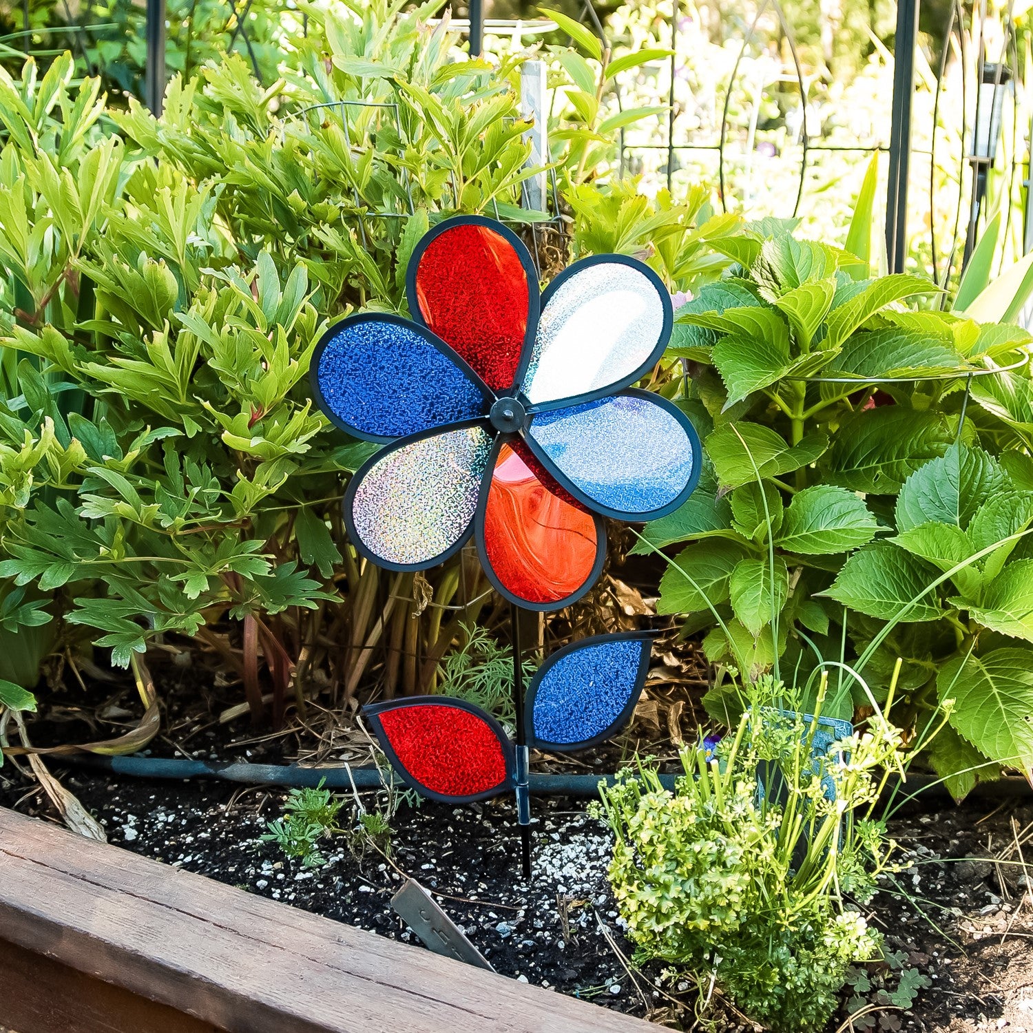12-inch red, white, and blue sparkle flower spinner rotating in a garden, showcasing its Mylar petals and sturdy fiberglass pole.