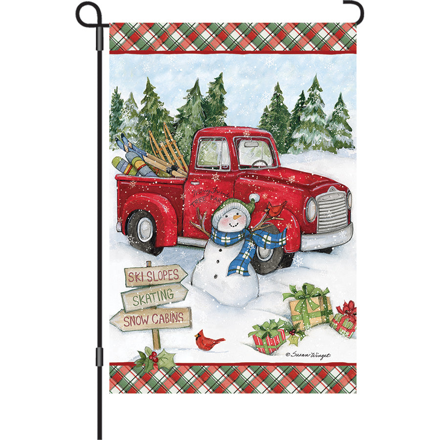 13 in. Elite Oversized Garden Flag with a vibrant red truck snowman design, displayed on a garden flagpole in a winter setting.