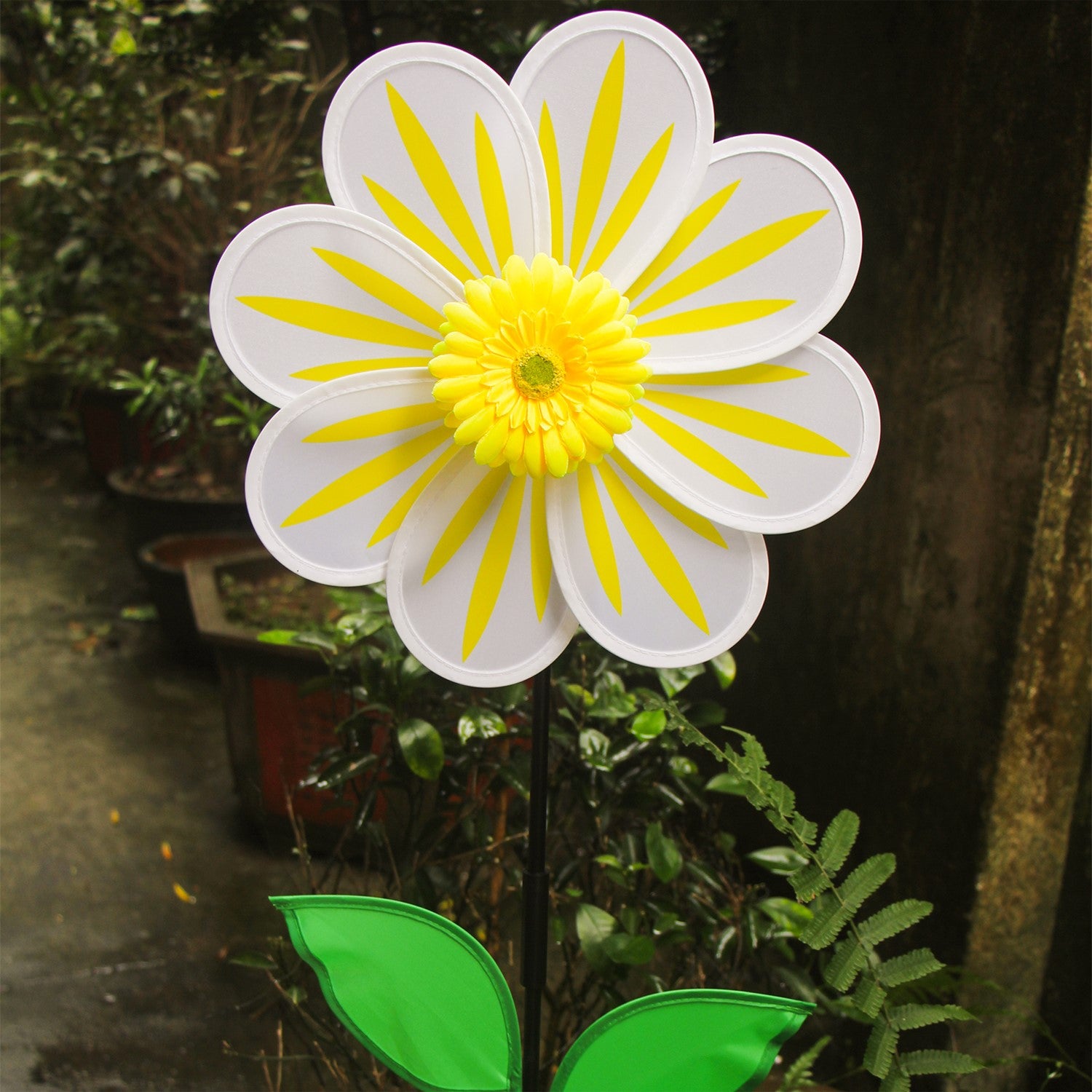 A 13-inch White Daisy Flower Spinner spinning in a garden, featuring an 8-petal design with a white floral motif against a natural backdrop.
