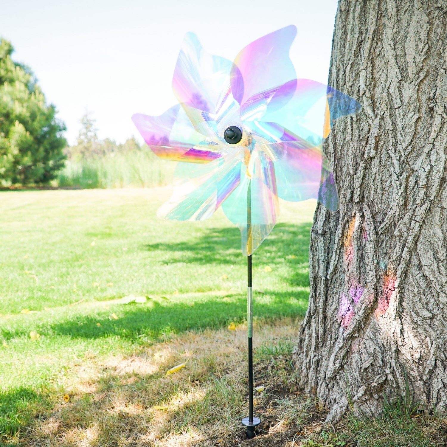 18-inch iridescent pinwheel spinner with colorful Mylar petals spinning on a garden pole, reflecting light in a vibrant outdoor setting.