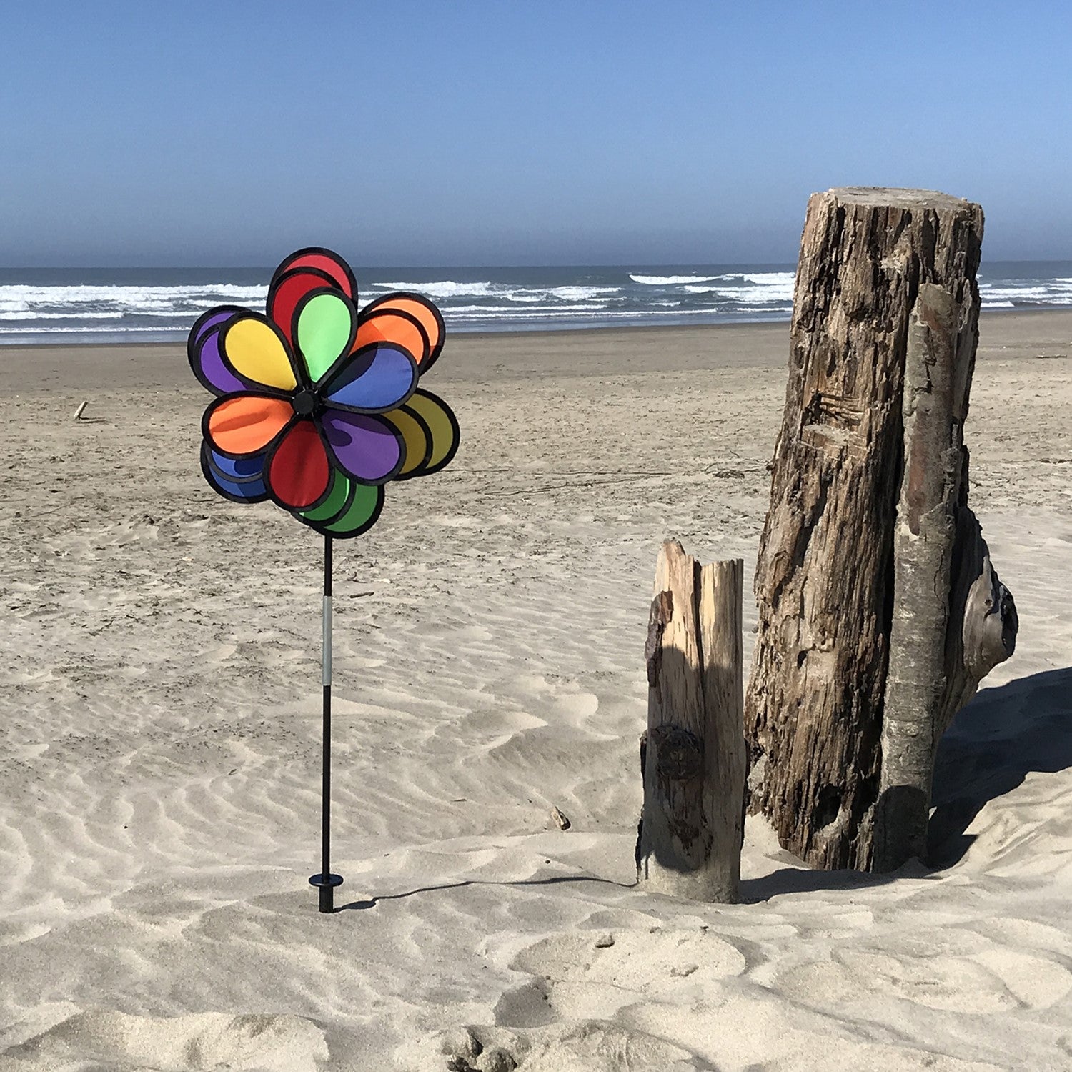 18 Petal Triple Flower Spinner with vibrant rainbow colors and rotating flower petals displayed in a garden on a sturdy pole.
