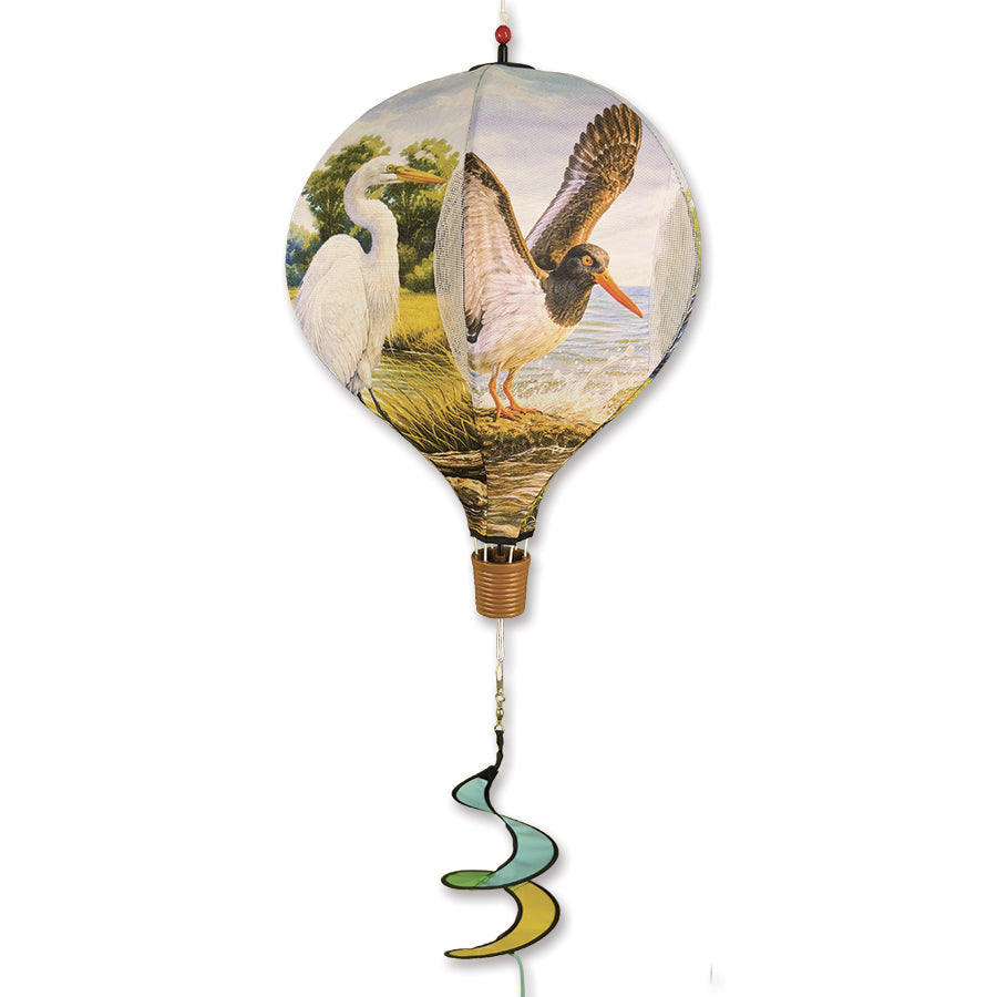 19 in. Pop-Open Hot Air Balloon featuring Coastal Birds design, suspended outside gently spinning in the breeze among greenery.