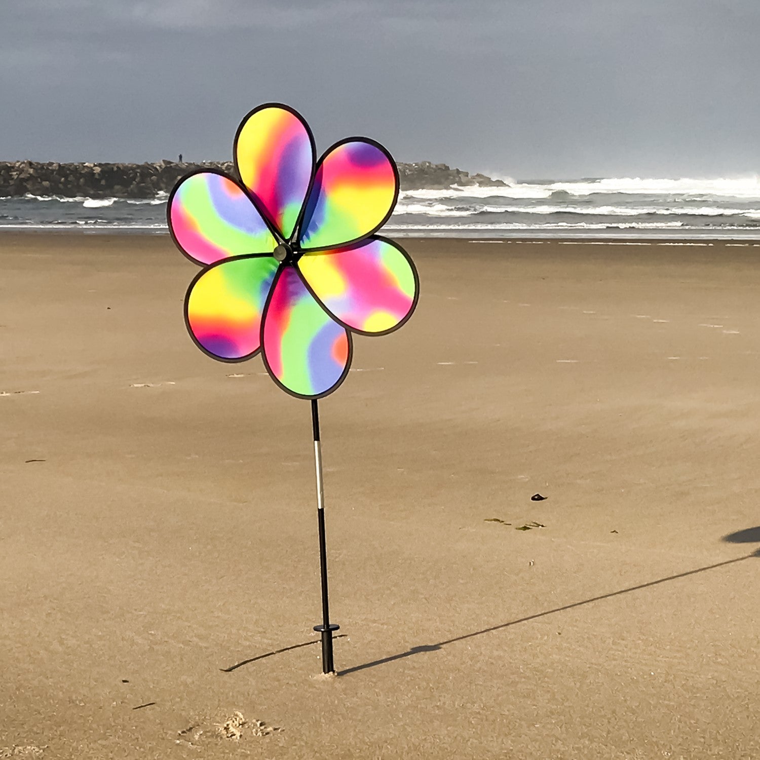 19-inch Jewel Flower Spinner with vibrant rainbow flower design, spinning gracefully in a garden setting under bright sunlight.