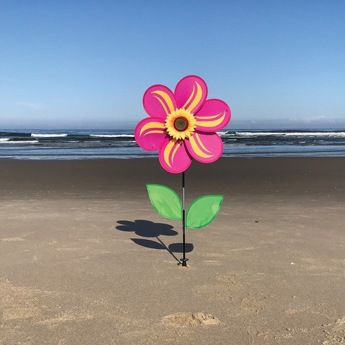 19-inch pink sunflower spinner with six petals, realistic sunflower center, and two green leaves, mounted on a sturdy fiberglass pole in a garden setting.