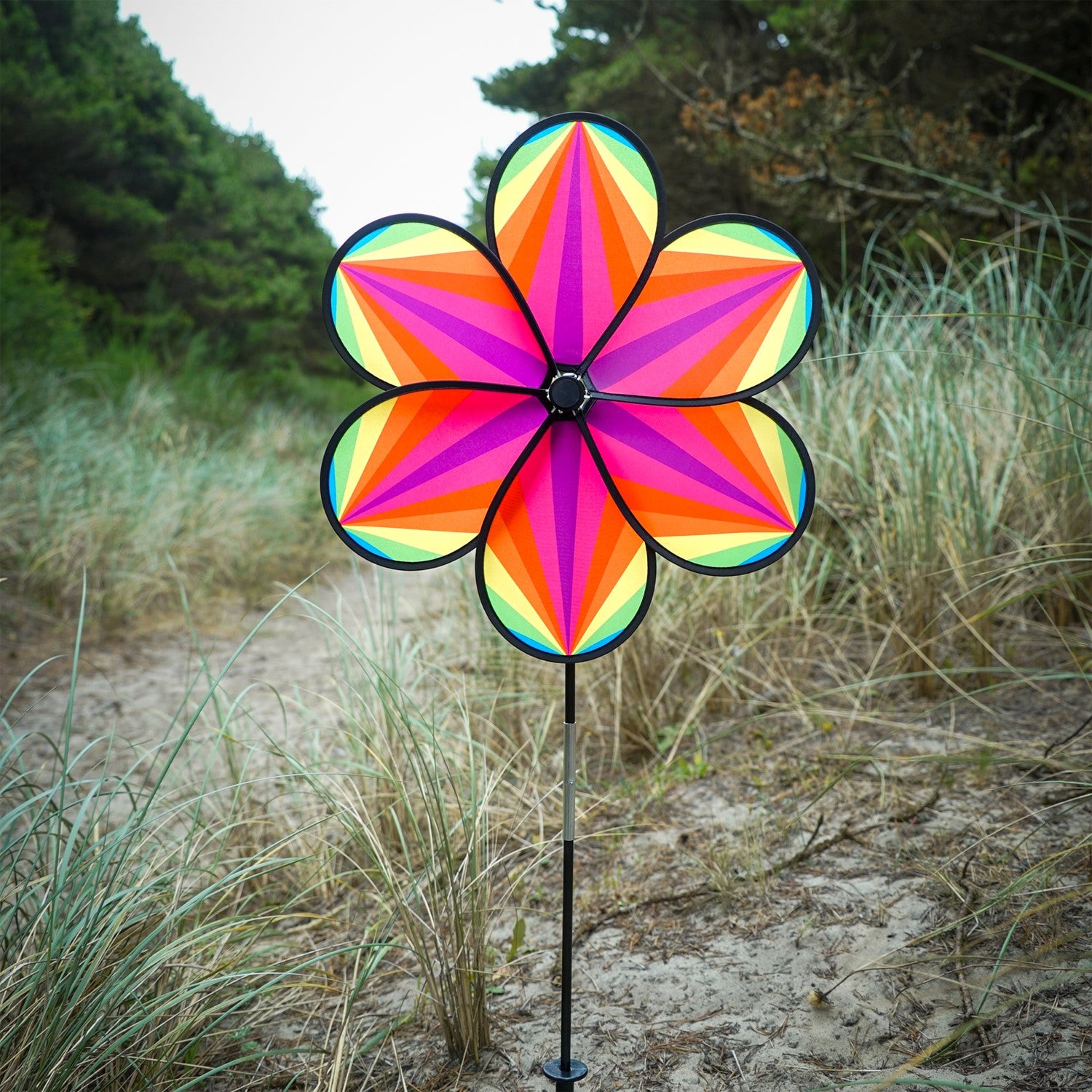 19-inch Rainbow Star Flower Spinner with colorful striped petals spinning in the breeze, displayed in a garden setting.