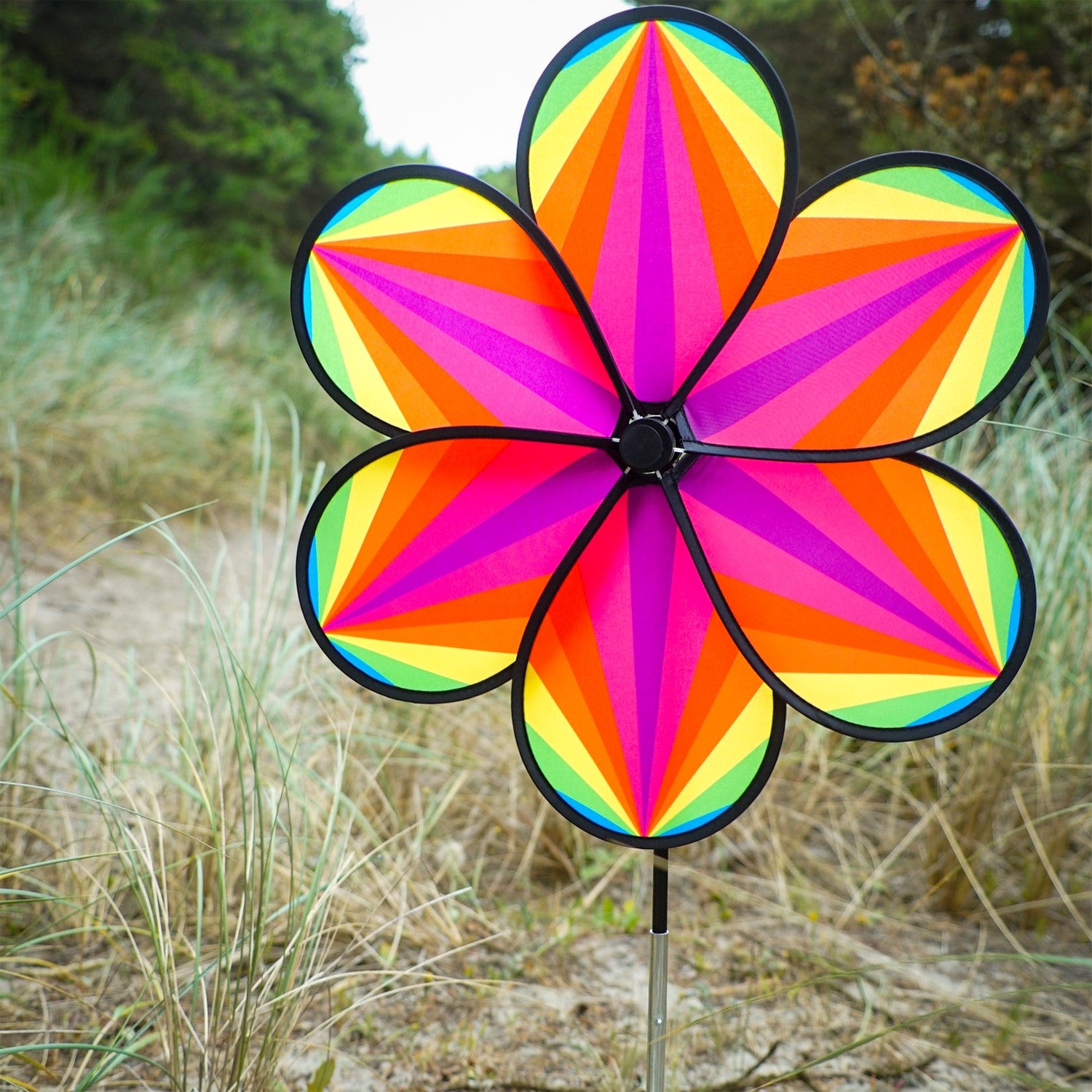 19-inch Rainbow Star Flower Spinner with colorful striped petals spinning in the breeze, displayed in a garden setting.