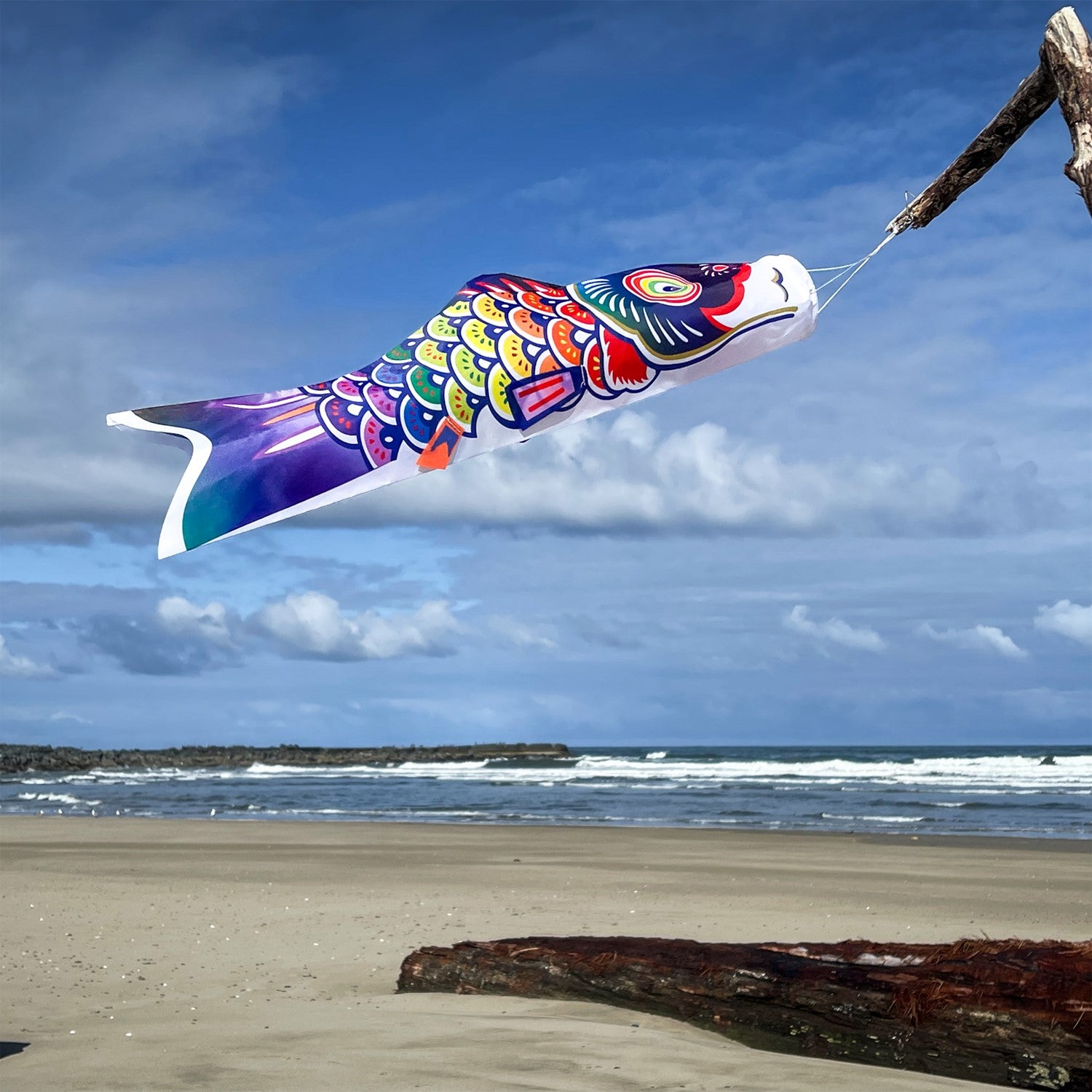 2' Spectrum Koi Fishsock in vibrant rainbow colors hanging from a garden hook in a garden setting, capturing the breeze effortlessly.