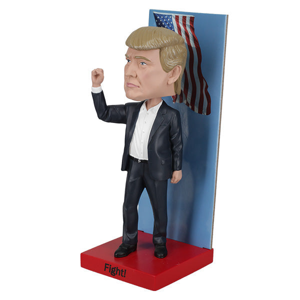 2025 Inauguration Limited Edition Donald Trump Bobblehead featuring a raised fist and American flag backdrop displayed on a shelf.