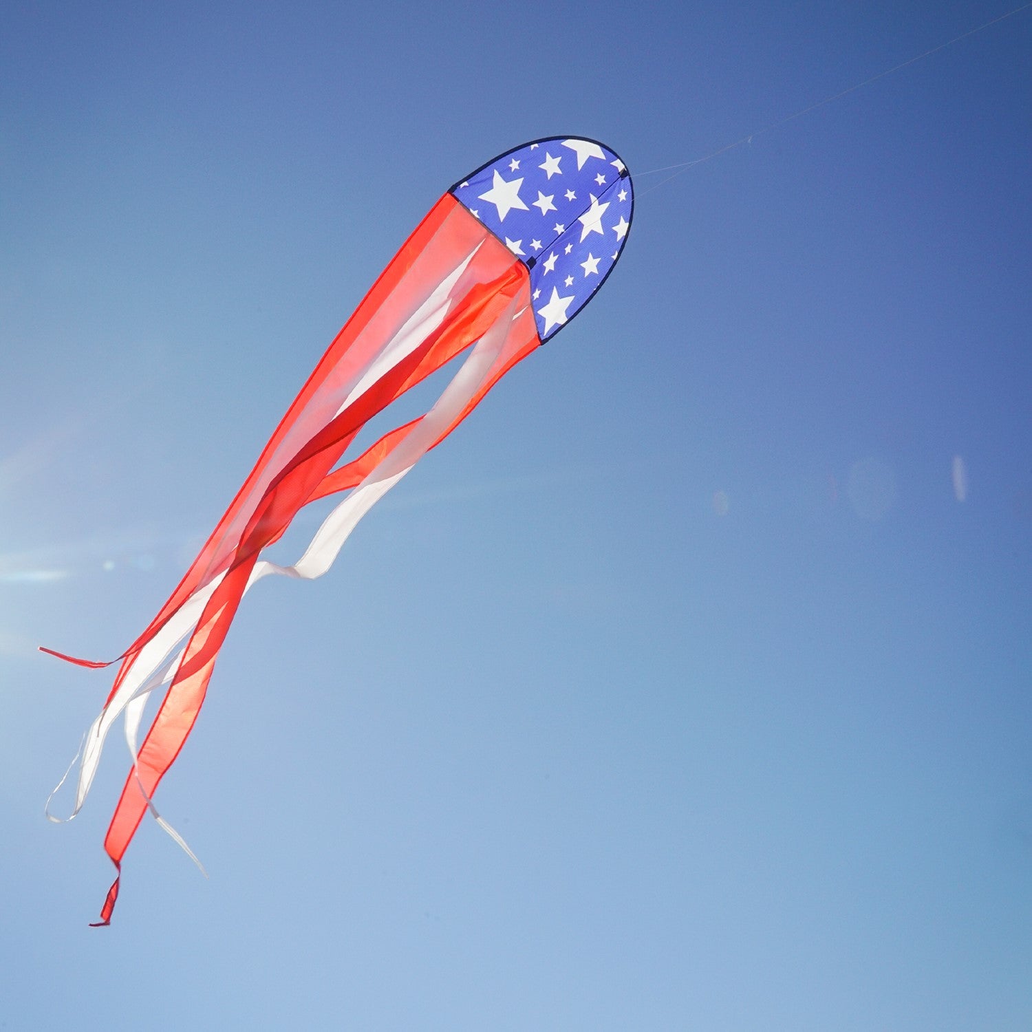 22" Patriot Dancing Dragon Kite with stars and stripes design soaring through the sky during a sunny outdoor event with tails flowing.