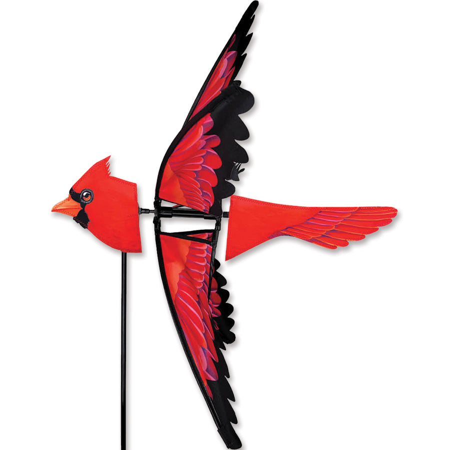 23 in. North American Cardinal Spinner featuring vibrant red and black colors, spinning gracefully in a garden setting against a clear blue sky.