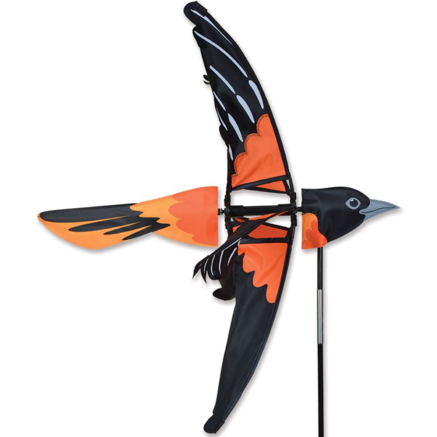A vibrant 24 in. Oriole Spinner twirling gently in the wind, showcasing its colorful bird design in a garden setting.
