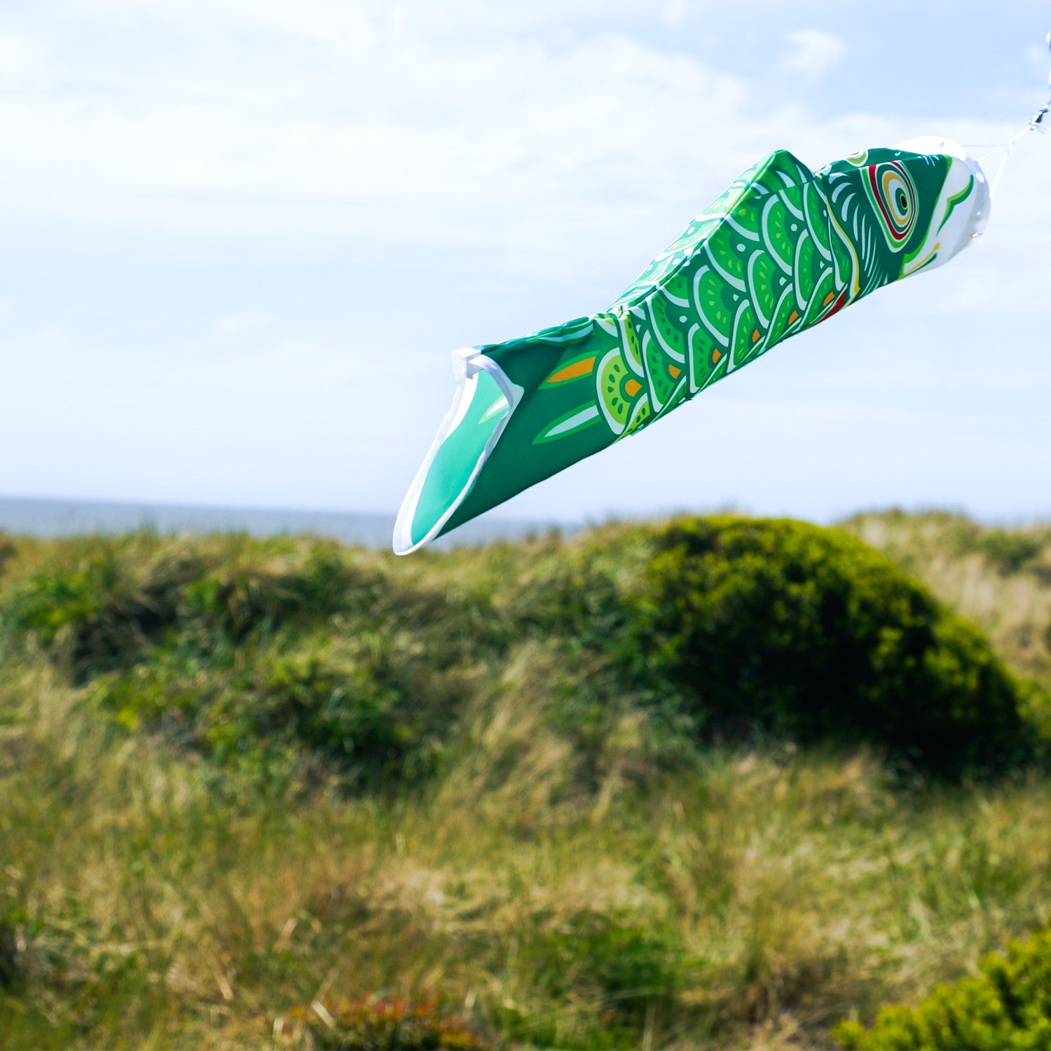 24\" Green Koi windsock featuring intricate fish design, fluttering in the breeze, showcasing vibrant colors against a clear sky backdrop.