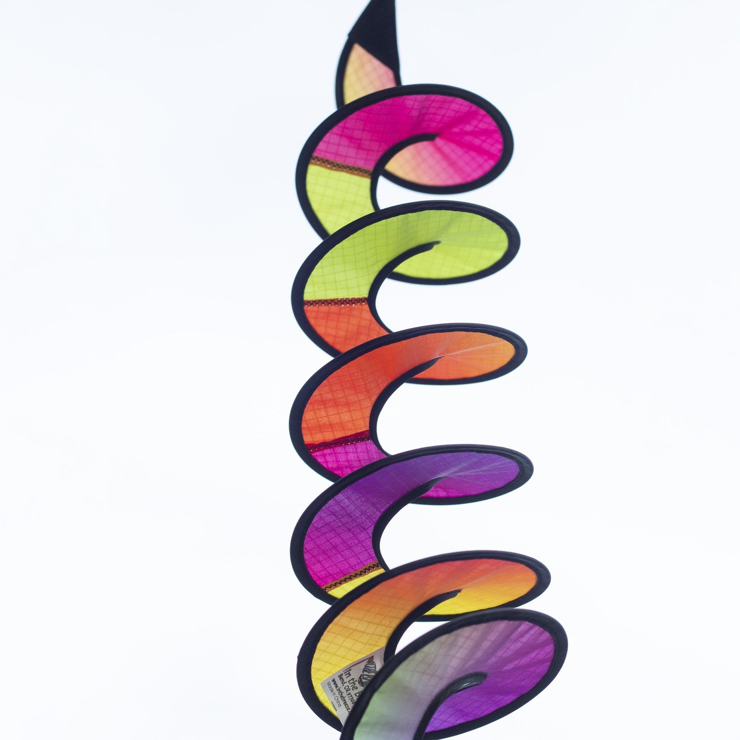 24-inch Jewel Curlie featuring a colorful rainbow graphic, hanging elegantly in an outdoor garden setting, moving gently in the breeze.