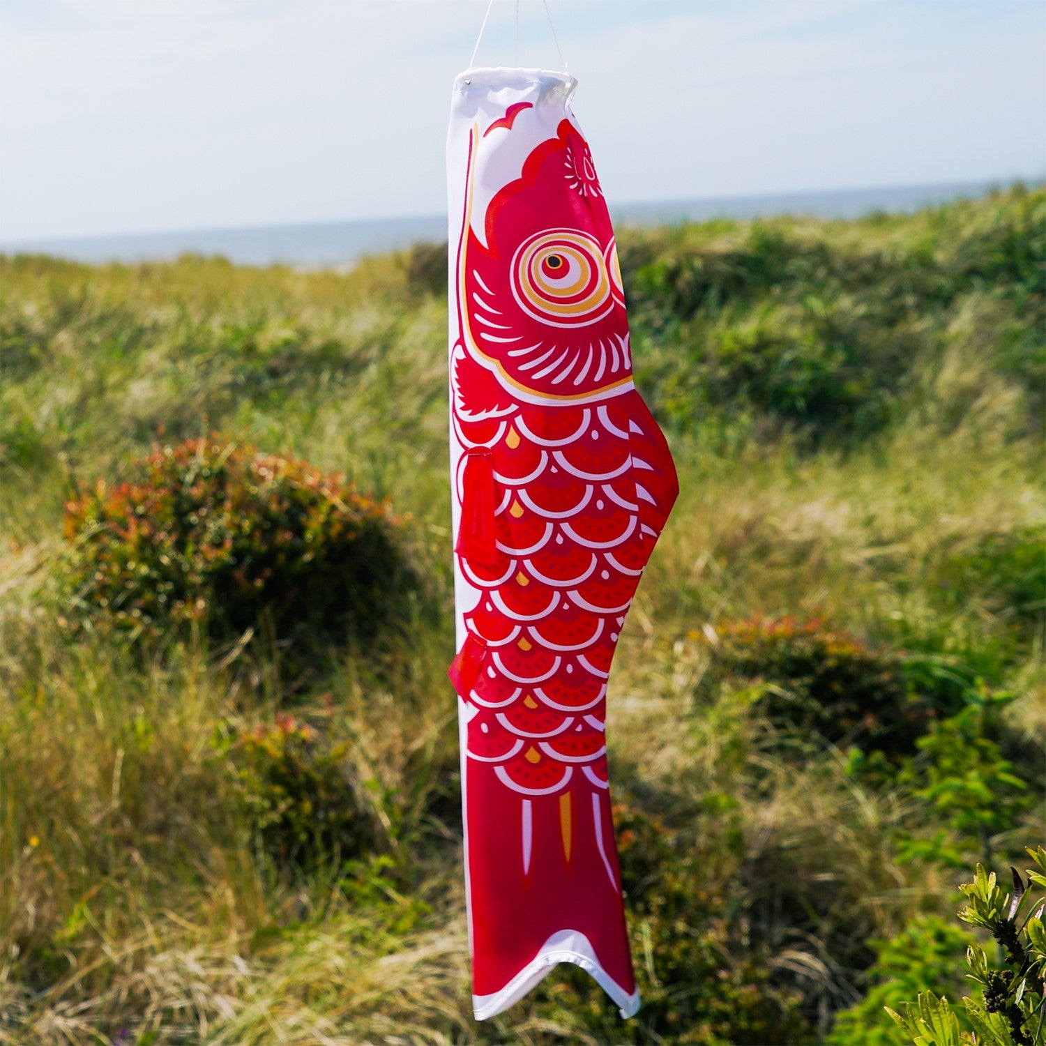 24-inch Red Koi windsock hanging outdoors, featuring a vibrant red koi fish design fluttering in the breeze against a clear sky.