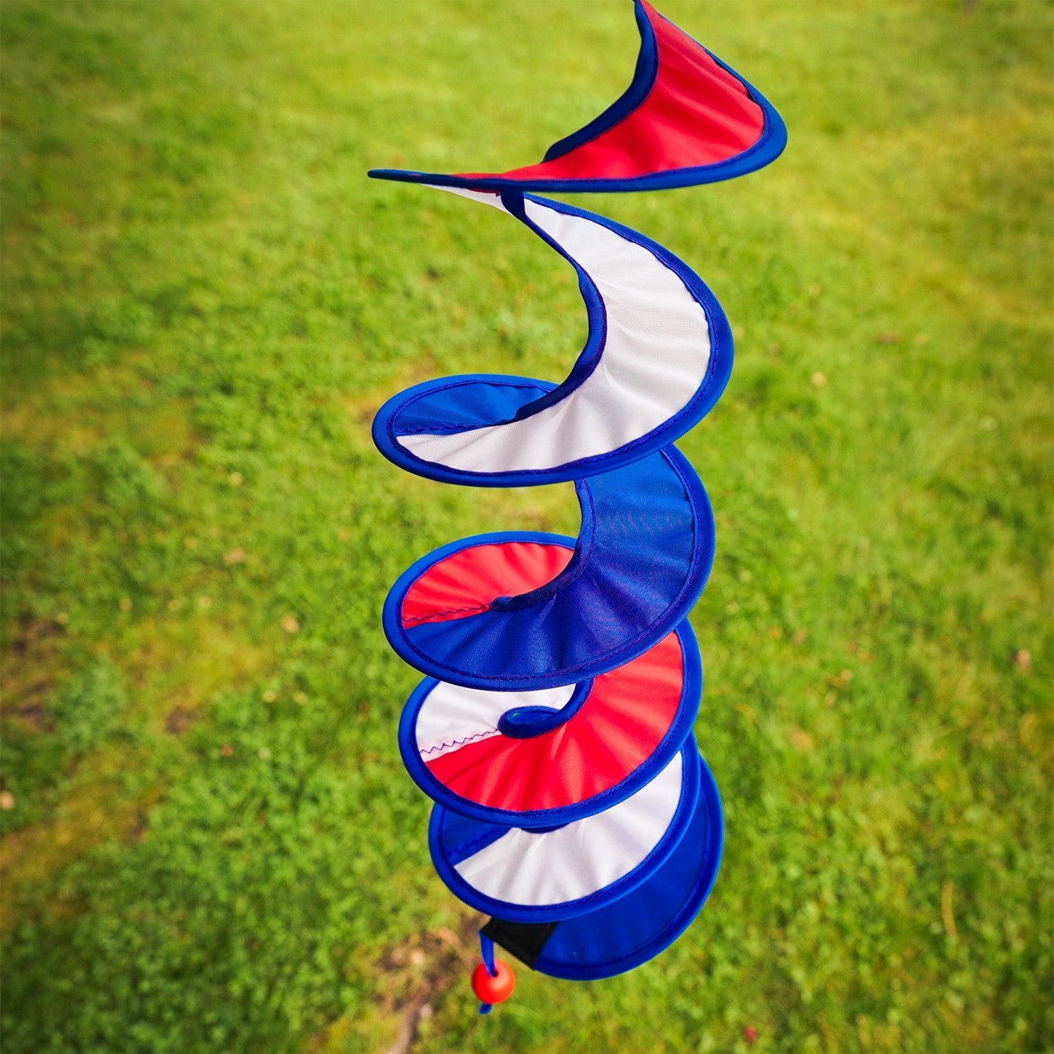 24-inch Red, White and Blue Curlie spinner hanging outdoors, displaying a vibrant spiral design in patriotic colors, gently swirling in the breeze.