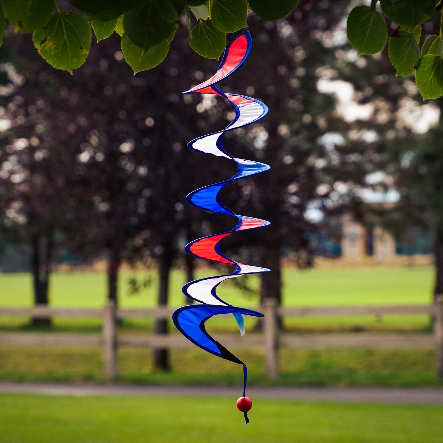 24-inch Red, White and Blue Curlie spinner hanging outdoors, displaying a vibrant spiral design in patriotic colors, gently swirling in the breeze.
