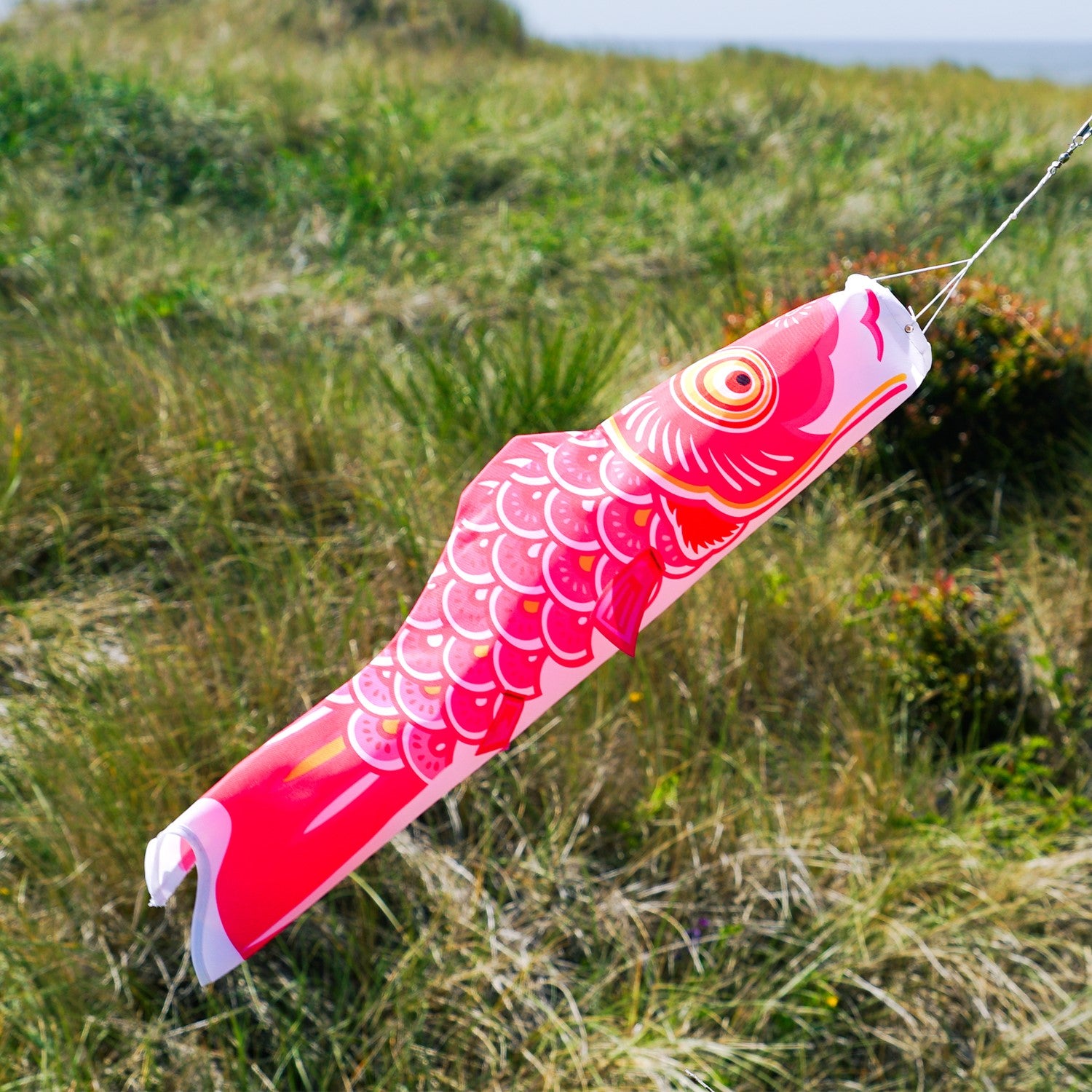 Colorful 24" Pink Koi windsock hanging outdoors, showcasing its vibrant design and fluttering in the breeze.