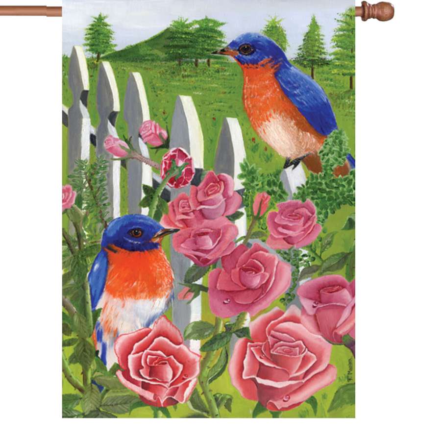 Illuminated 28 in. Bluebird & Rose flag showing a vibrant bluebird on a blooming rose, displayed outdoors in garden setting.