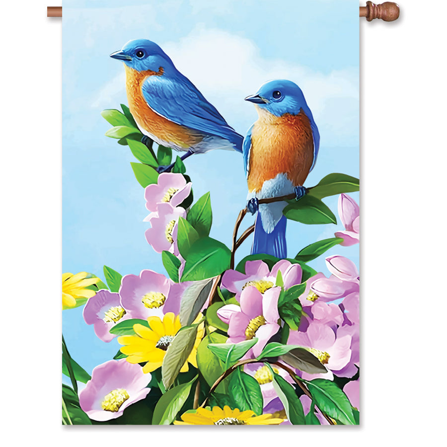 28 in. Floral Bluebirds flag featuring vibrant bluebird designs surrounded by flowers, displayed on a flagpole in a sunny garden setting.