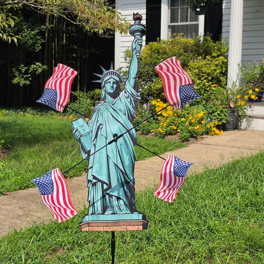 38 in. WhirliGig Spinner - Lady Liberty featuring a vibrant USA flag design, spinning gracefully in a garden setting under blue skies.