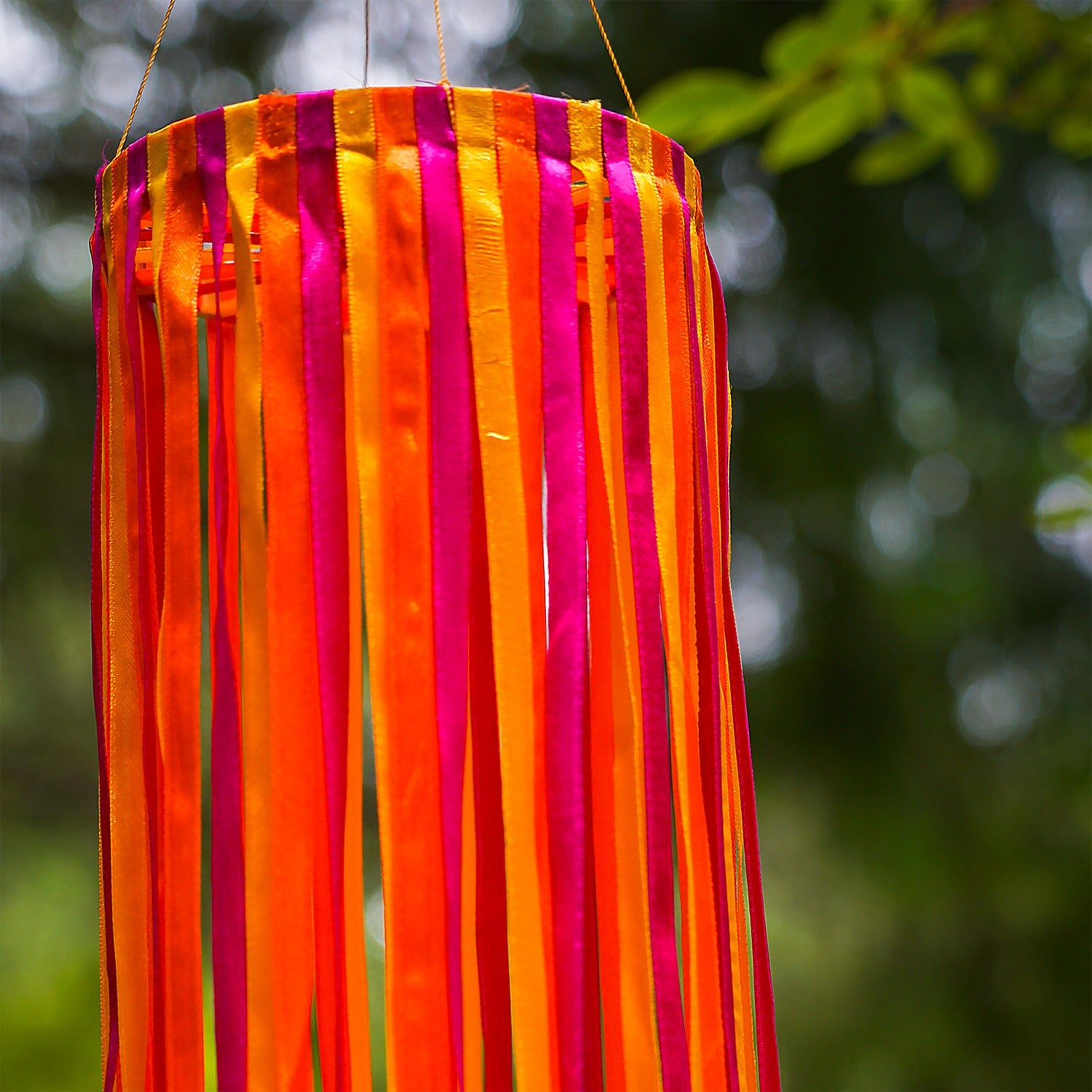 39-inch Sunset Ribbon Windsock featuring vibrant satin ribbons in fuchsia, orange, and yellow displayed outdoors, swaying gently in the wind.