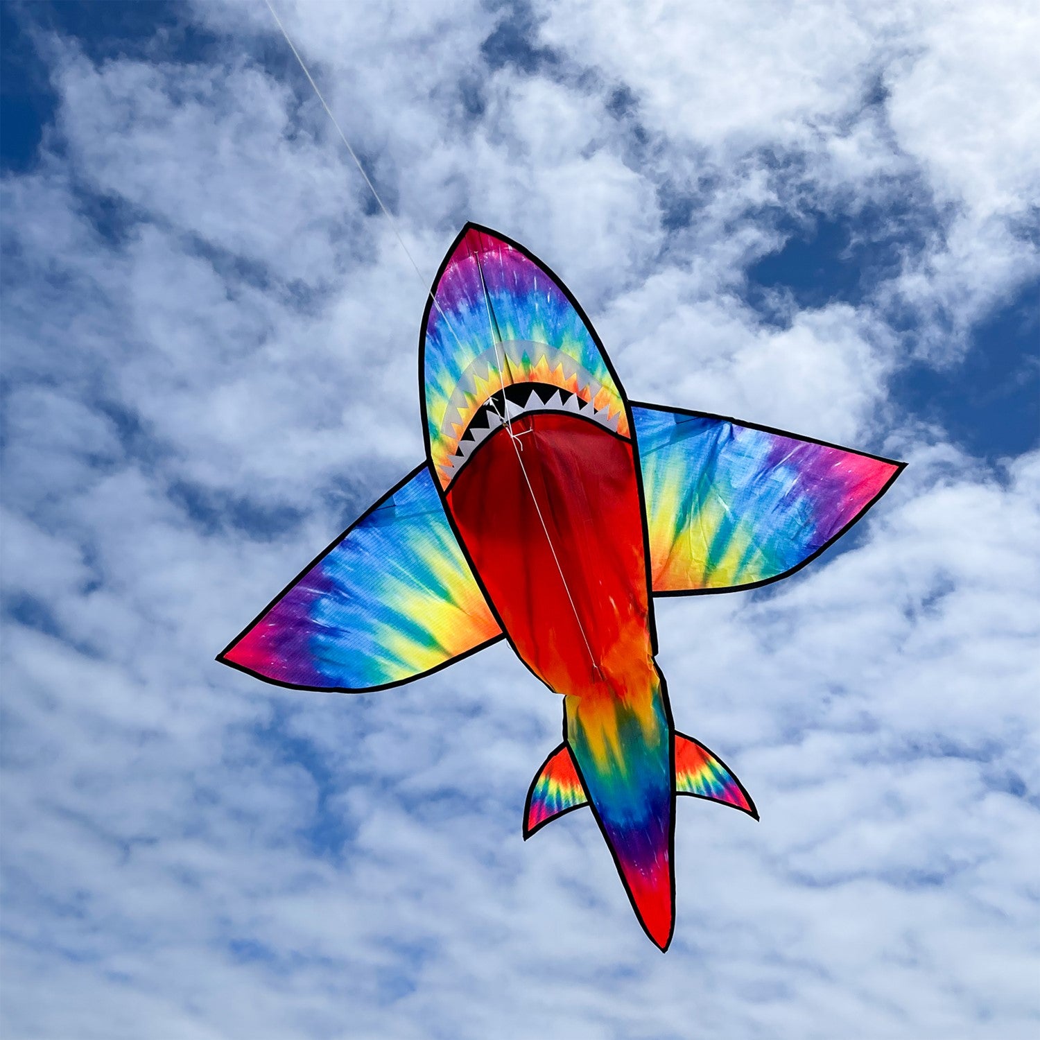 5-foot 3D Tie Dye Shark Kite flying high against a blue sky, showcasing its vibrant colors and fun design as it swims through the air.