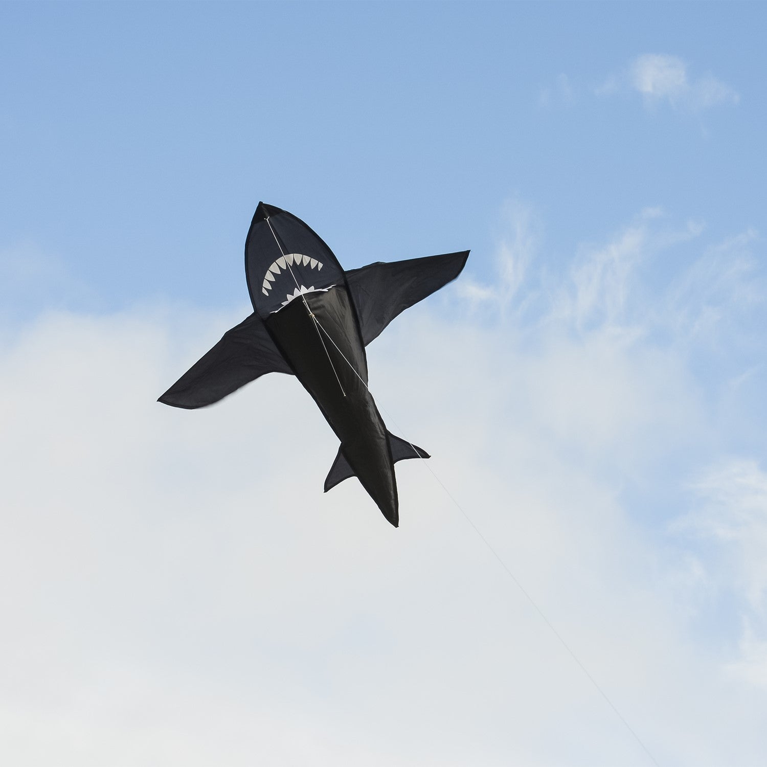 A vibrant 4' 3D Shark Kite soaring across a blue sky, showcasing its toothy design and dynamic motion as it is flown by a family enjoying the outdoors.