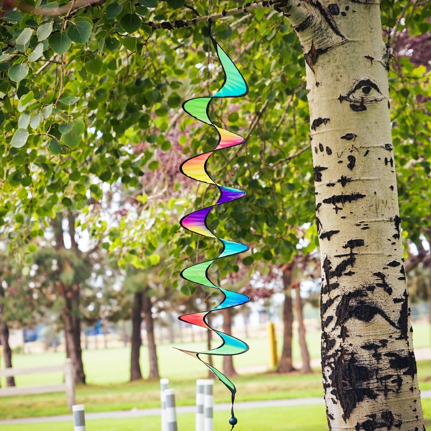 48-inch Jewel Curlie featuring a rainbow design, elegantly swirling and suspended in an outdoor garden setting.