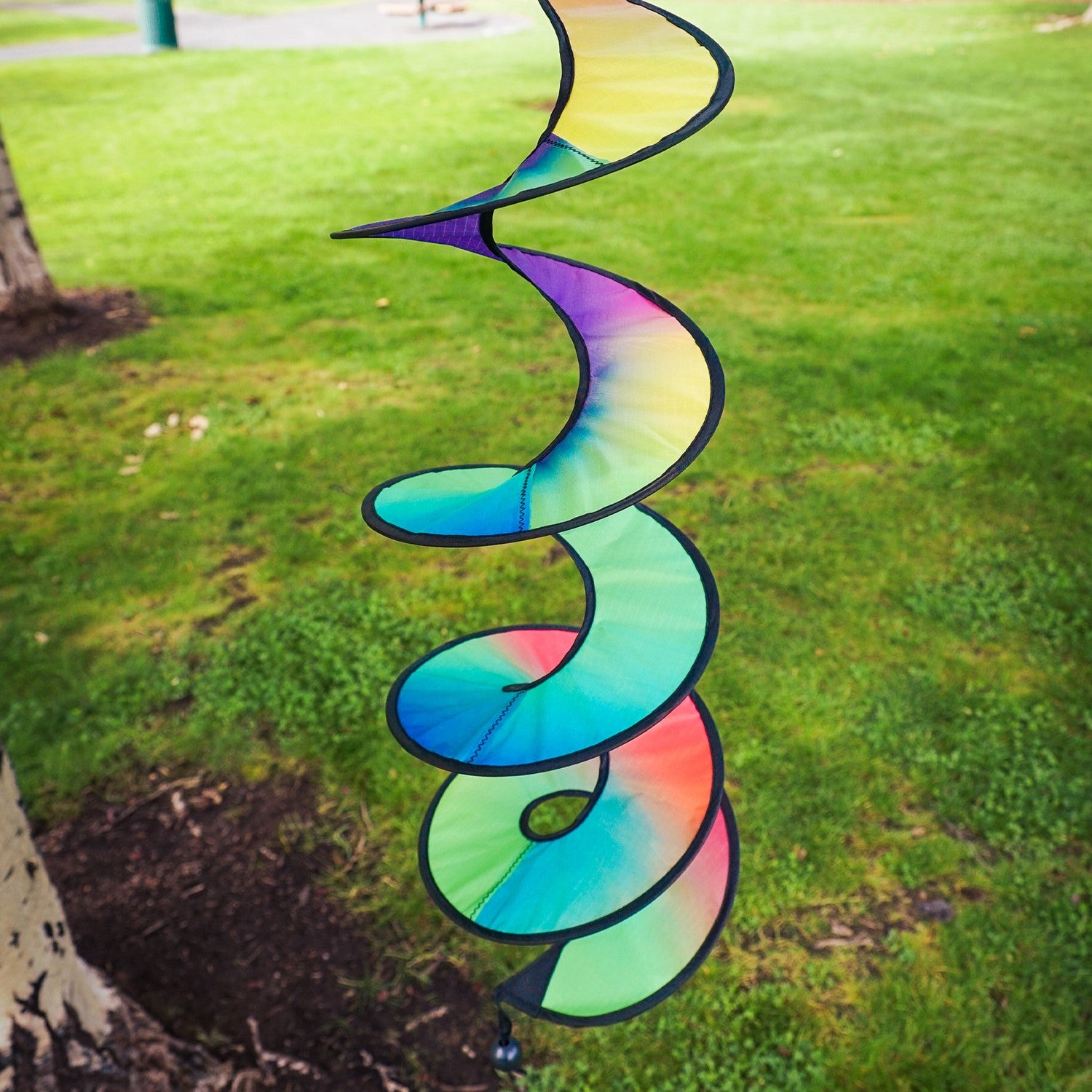 48-inch Jewel Curlie featuring a rainbow design, elegantly swirling and suspended in an outdoor garden setting.