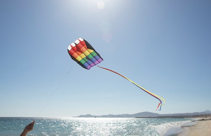 5.0 Rainbow Stripes Air Foil kite soaring in a clear blue sky, showcasing colorful appliques and attached tails in flight.