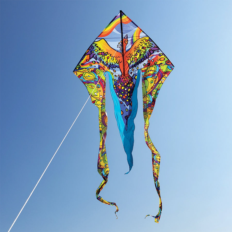 6.5 ft. Flo-Tail Delta Kite with rainbow bird design flying high against a clear blue sky, showcasing colorful flowing tails.