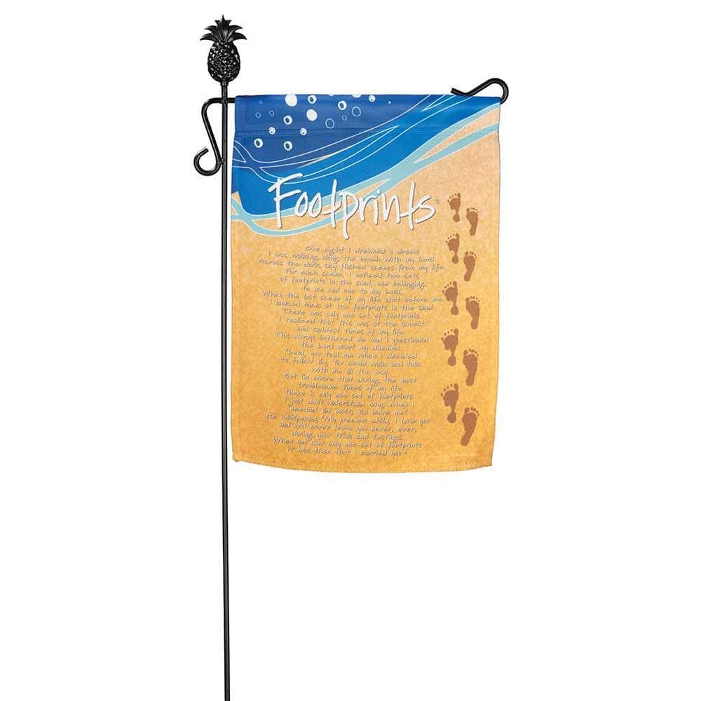 Main image of 13x18 Footprints garden flag hanging from a decorative metal yard pole showing a sandy footprint motif and calm beach-inspired tones in a green garden setting.