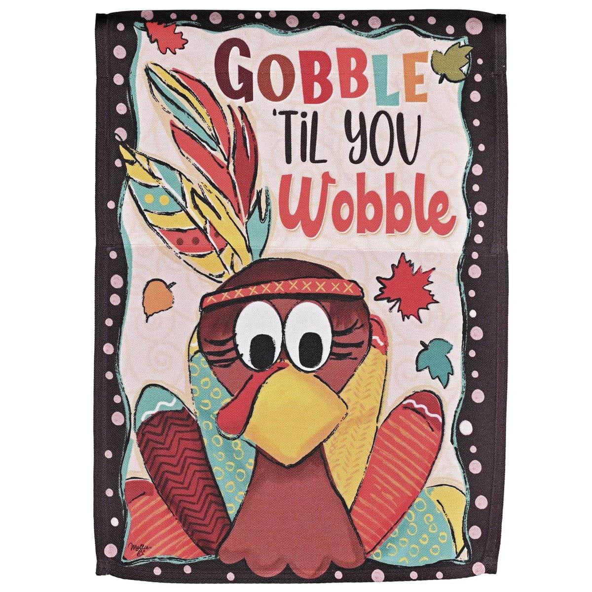 Printed Gobble Til You Wobble Turkey flag hung on a porch railing with autumn leaves, pumpkins, and harvest decorations in the background