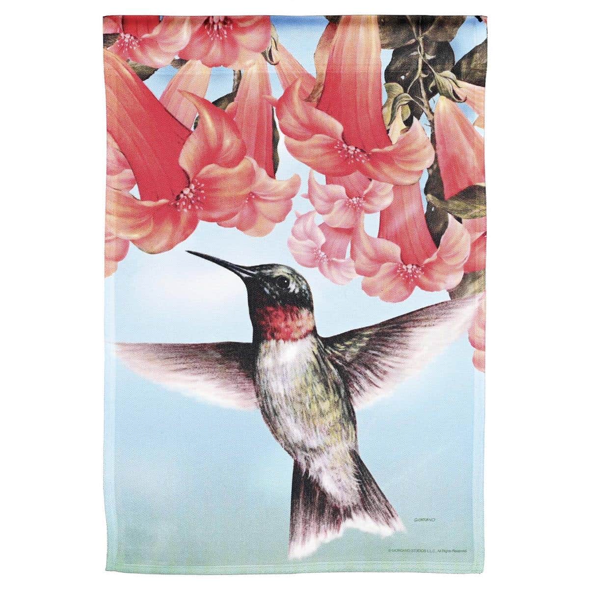 Printed 13x18 hummingbird garden flag with vivid hummingbird and floral artwork on durable polyester, shown hanging from a standard garden flag pole in a flower bed.