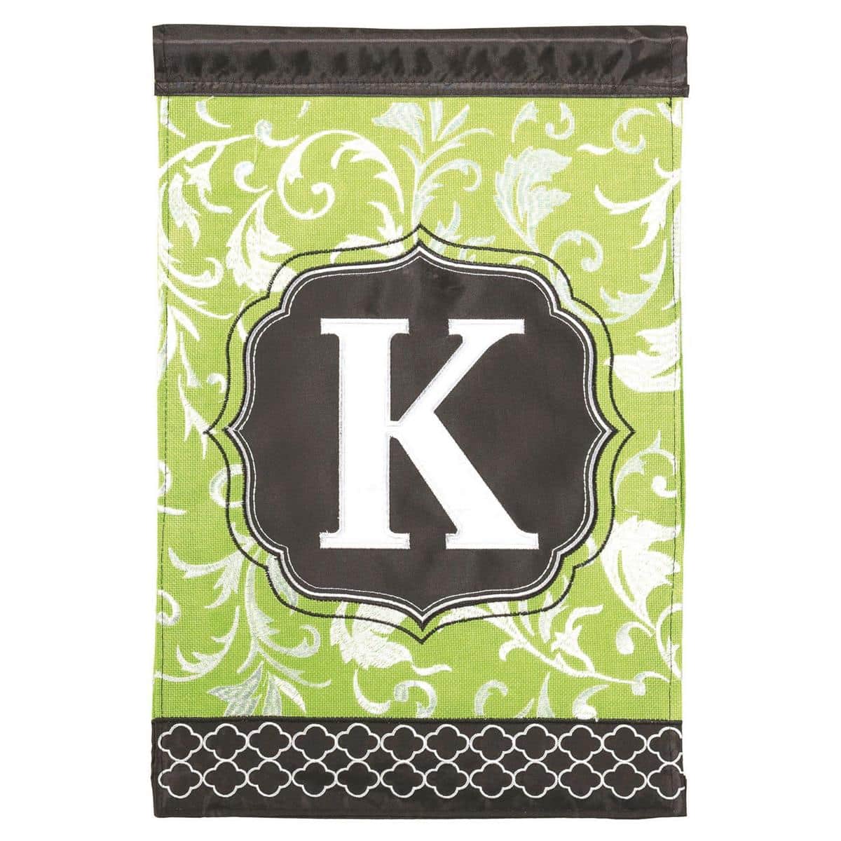Green and black 13x18 double applique garden flag with bold letter K monogram, two-sided stitching visible, displayed on a front yard stand by a walkway