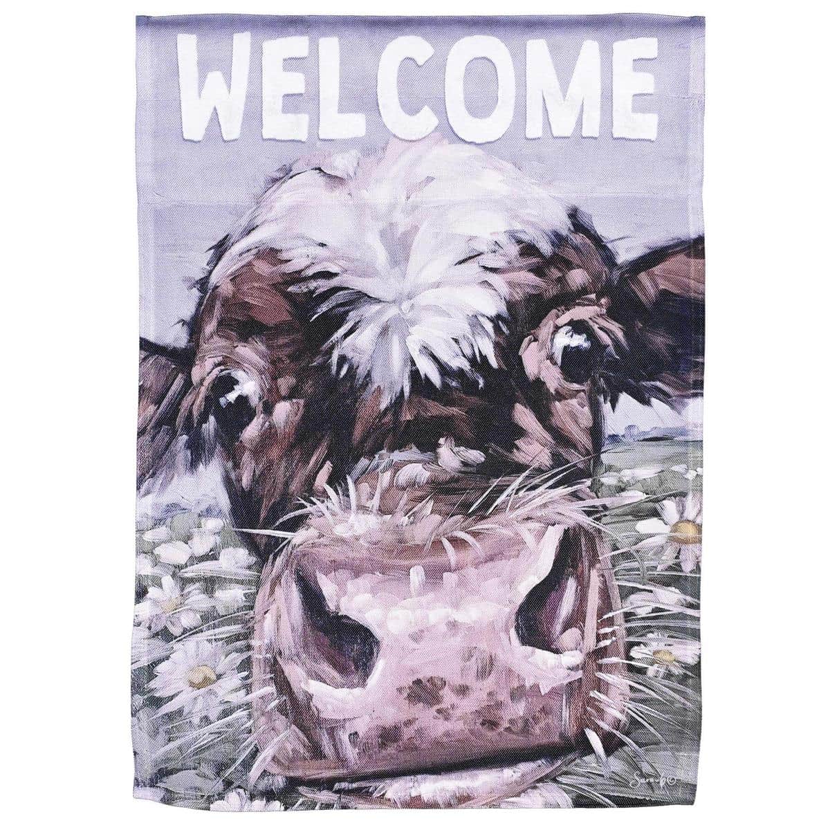 Main product image of a 13x18 Welcome Cow Garden Flag featuring a printed smiling cow with floral accents and a visible welcome message, shown displayed on a black metal shepherd hook in a flower bed near a porch, capturing scale and color for online shoppers.