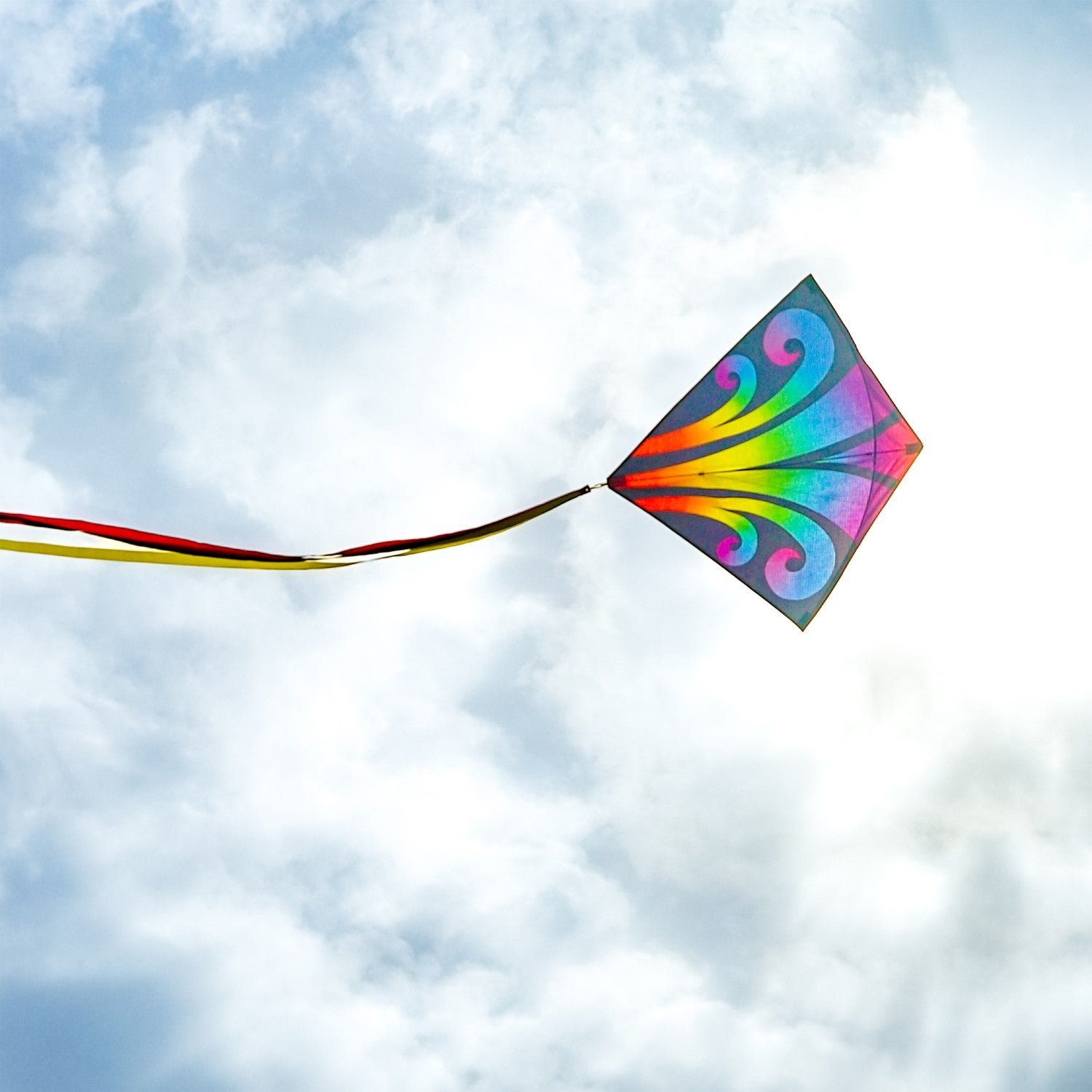 Aurora 30-inch diamond kite featuring vibrant colors and tails, soaring against a clear blue sky, captured in a fun outdoor setting.